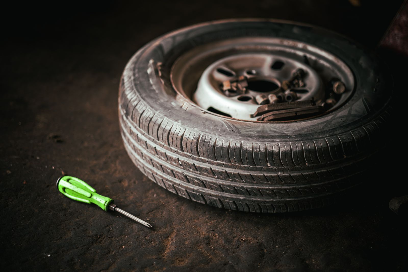 A part-worn tyre standing on a concrete workshop floor with a screwdriver beside it