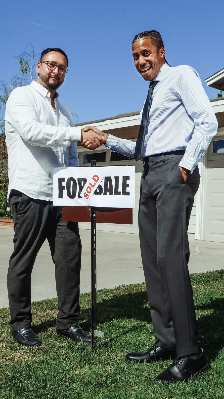 Two men shaking hands outside a house beside a sold board
