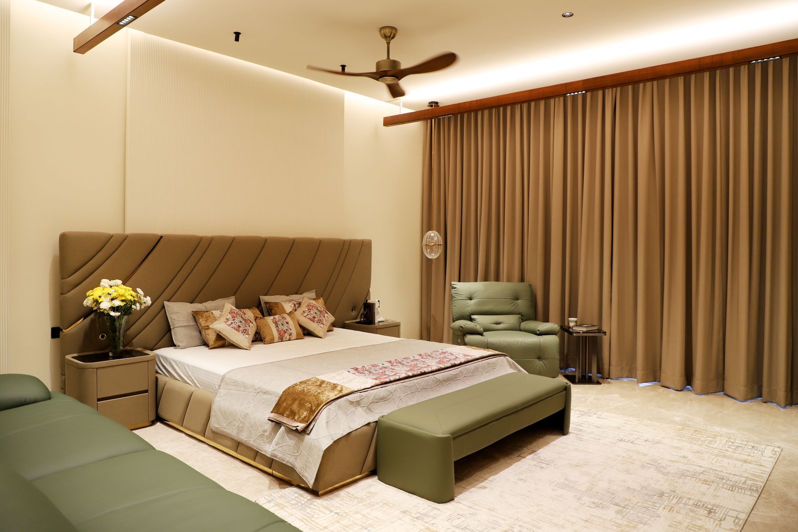 A principal bedroom with an upholstered bed, full-height curtains and a seating corner