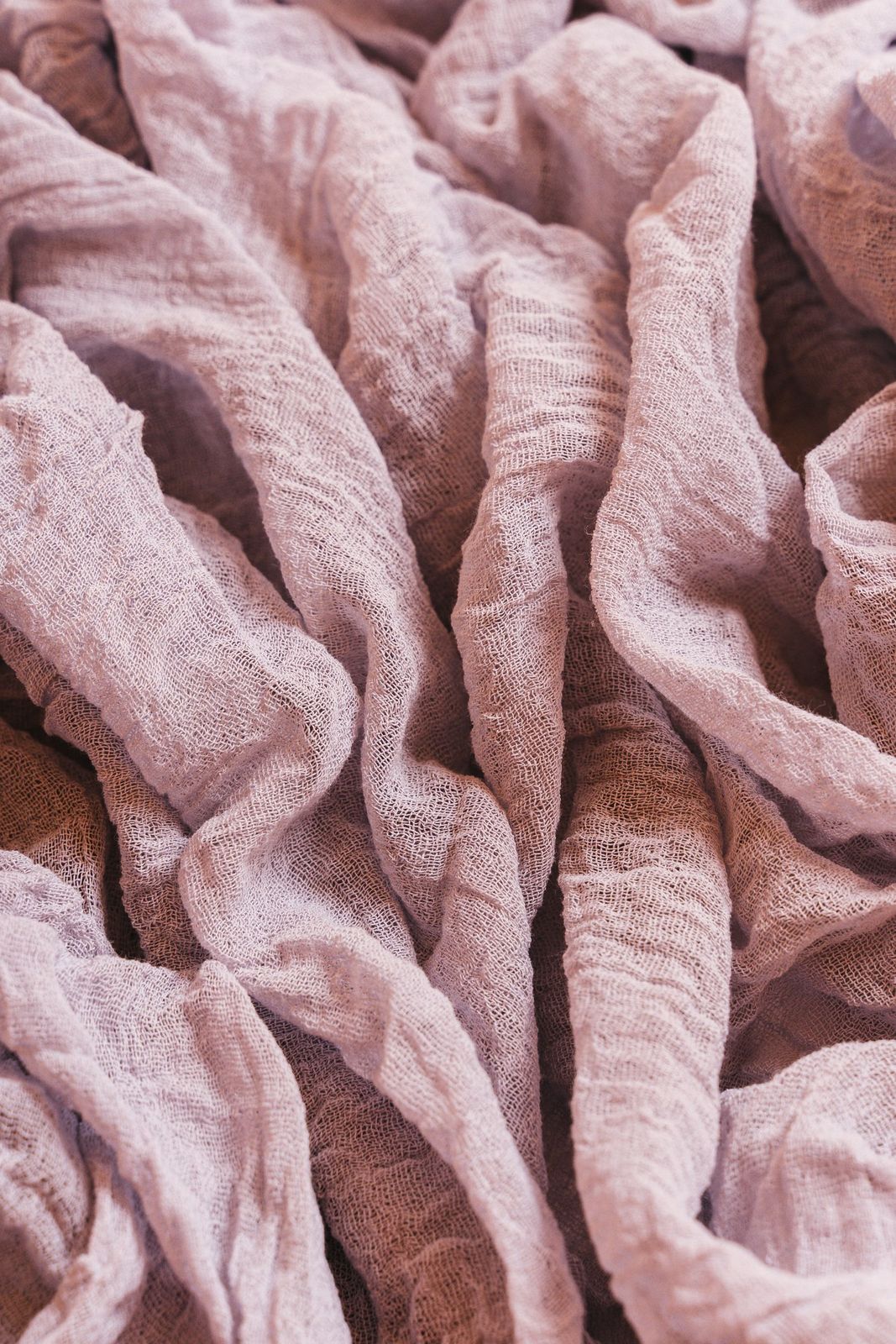 A washed linen throw in soft plum, loosely folded on a bench